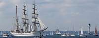 Segelschulschiff Gorchf Fock Windjammerparade Ein weißes, dreimastiges Segelschiff in See umgeben von mehreren kleinen, weißen Sportbooten.