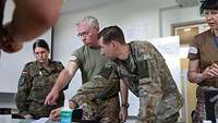 Two female and two male soldiers of different nations stand around a table on which a map is lying.