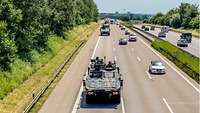 Eine Kolonne von Fahrzeugen fährt auf der Autobahn neben zahlreichen zivilen Fahrzeugen.