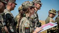 Soldaten stehen in einer Gruppe zusammen. Eine litauische Soldatin hält eine Karte in der Hand.