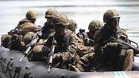 Soldaten sitzen mit Helm, Schwimmweste und Waffe im Schlauchboot