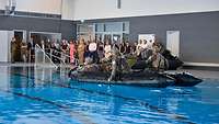 In einem Schwimmbecken sitzen Soldaten mit Hund in einem Schlauchboot.