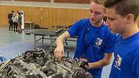 Zwei junge Männer arbeiten an einem Motorblock