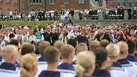 Eine Gruppe von Menschen mit Fotoapparaten; im Vordergrund untere Bildhälfte Soldaten in Matrosenuniform.
