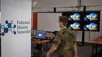Ein Soldat geht während der Übung CWIX an einem Aufsteller „Federated Mission Networking“ vorbei
