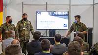 Eine Gruppe Soldaten und Zivilisten führt ein Treffen vor einem Computer mit der Aufschrift CWIX durch