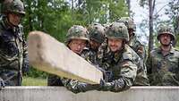 Mehrere Soldaten hieven einen Holzbalken über ein Hindernis.