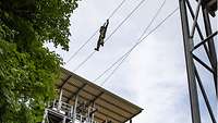 Ein Soldat hangelt sich an einem Seilsteg in 15 Meter Höhe von einem Kletterturm zum nächsten.