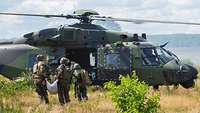 Vier Soldaten tragen einen Verwundeten auf einem weißen Bergetuch zu einem Rettungshubschrauber.