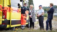 Vier Personen stehen an der Seite eines Rettungsdienstfahrzeuges und blicken in den Innenraum des Fahrzeugs