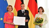 Eine Frau und ein Mann in Feuerwehruniform halten eine Urkunde. Der Mann trägt eine Medaille an der Uniform.