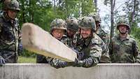 Mehrere Soldaten hieven einen Holzbalken über ein Hindernis