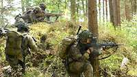 Liegend und kniend im Wald besprechen Soldaten ihr Vorgehen.