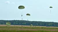 Auf einer Wiese landen mehrere Fallschirmjäger.