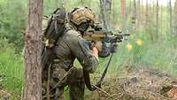 Ein Soldat lehnt an einem Baum und feuert mit seiner Waffe.