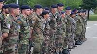 Deutsche und französische Soldaten stehen in einer Formation auf einem Appellplatz.