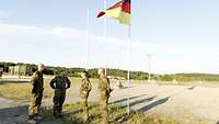 Ein Militärpfarrer ist im Gespräch mit drei Soldaten vor einer Flagge