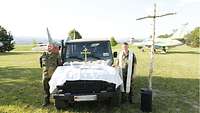 Ein Soldat und ein Militärpfarrer stehen neben einem Einsatzfahrzeug, dessen Motorhaube zum Altar umfunktioniert ist