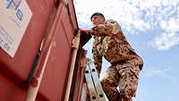 Ein Soldat mit schwarzem Barett klettert über eine Leiter auf das Dach eines Seecontainers