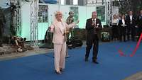 Eine Frau und ein Mann stehen in einer Halle auf einem blauen Teppich und posieren für die Kamera.