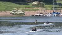 Zwei Fallschirmspringer sind im Wasser gelandet. Zwei Schlauchboote bewegen sich schnell auf sie zu.