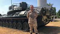 Ein Soldat steht in einem Flecktarnanzug vor einem Panzer.