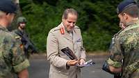 Lieutenant General Copinger-Symes halt einen Flyer auf dem er selber abgebildet ist. Um ihn herum sind Soldaten.