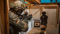Ein Soldat stürmt in einen beleuchteten Raum und zielt mit dem Gewehr auf eine Pappscheibe.