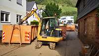 Ein Bagger der Bundeswehr lädt in einer Straße Müll in einen Container