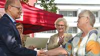Zwei Personen geben sich nach einer Ehrung die Hand, dahinter steht Christine Lambrecht und applaudiert