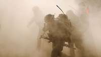 Soldaten mit Rucksäcken und Gewehren stürmen durch eine Staubwolke.