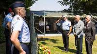 Drei Männer stehen vor einem Gedenkstein, der von zwei Soldaten flankiert wird. Sie haben Kränze davor abgelegt