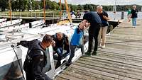 Mehrere Menschen stehen teilweise an der Pier und teilweise auf einem Boot.