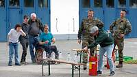 Eine Gruppe von Personen steht um eine Sitzbank, auf der mit Wasser gefüllte Plastikflaschen stehen.