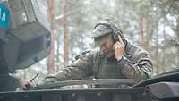 Ein Soldat schaut aus der Luke eines Panzers und funkt über ein Headset