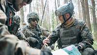 Deutsche und niederländische Soldaten hocken hinter einem Panzer. Ein Soldat erklärt den anderen etwas anhand einer Karte.