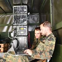 Zwei Soldaten arbeiten an Geräten auf einem Fahrzeug.