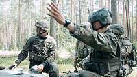 Soldaten hinter einem Panzer abgehockt. Einer zeigt den anderen die Richtung an.