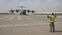Ein Soldat steht auf einem Rollfeld und weist ein heranfahrendes A400M Frachtflugzeug ein