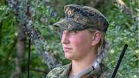 Man sieht eine Frau in Uniform mit zwei Funkgeräten, die eine Übung auf dem Truppenübungsplatz leitet.