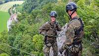Eine Soldatin seilt sich an einer Klippe ab, sie wird dabei von einem Soldaten mit einem Seil gesichert.