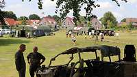 Im Hintergrund stehen zwei Zelte und im Vordergrund ein Fahrzeug und zwei Soldaten