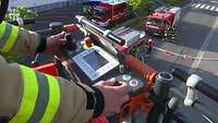 Feuerwehrmann bedient die Steuerung im Rettungskorb eines Leiterwagens, darunter Feuerwehrmänner und drei Feuerwehrfahrzeuge