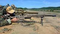 Ein Soldat schießt mit dem Maschinengewehr liegend im Gelände