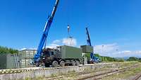 Ein Lkw steht neben den Gleisen. Ein blauer Kran hebt einen Container an.