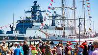 Viele Menschen stehen in einem Bundeswehr-Hafen und besichtigen mehrere Schiffe