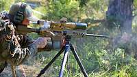 Ein Spotter schießt mit einem Gewehr, die auf ein Dreibein aufgelegt ist. Eine Hülse fliegt.