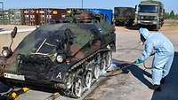 Ein Panzer wird von einem Soldaten in Schutzkleidung eingesprüht