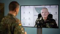 Ein Soldat ist per Live-Schaltung auf einem Monitor zu sehen, davor steht ein Soldat, der ihn interviewt.