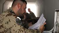 Ein Soldat sitzt in einem Bunker und hält einen Telefonhörer sowie einen Zettel in der Hand